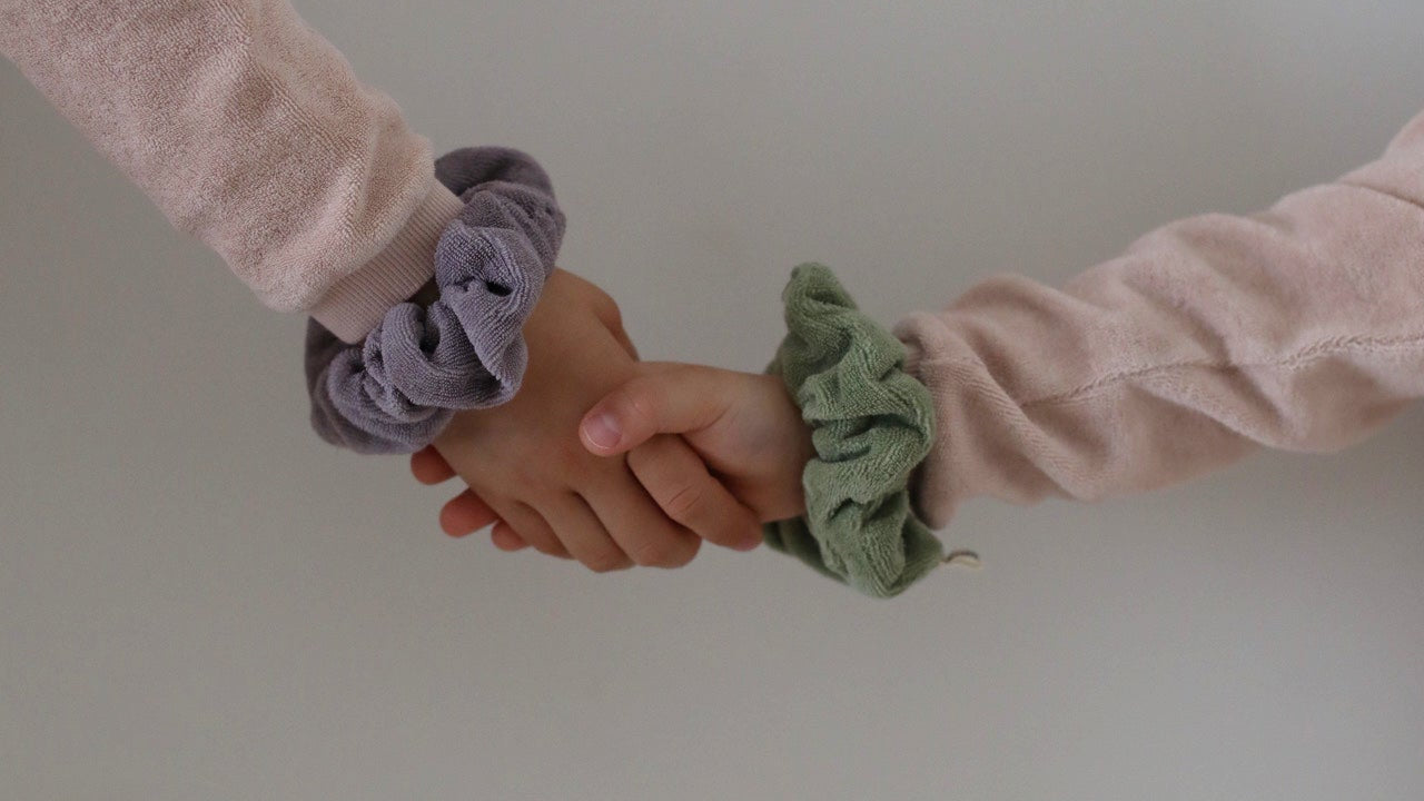Kinderhände halten einander fest, Frotteekleidung und Terry Scrunchies